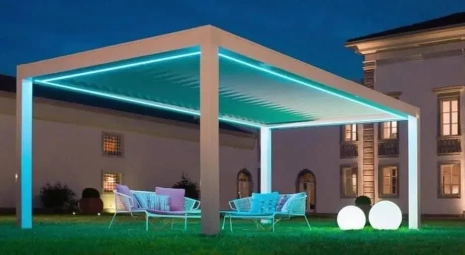 Алюминиевая пергола с бирюзовой LED-подсветкой над зоной отдыха у особняка вечером